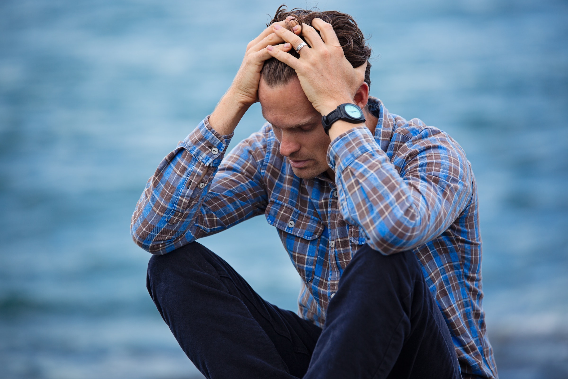 Frustrated man sitting down with his head in his hands on a blue background