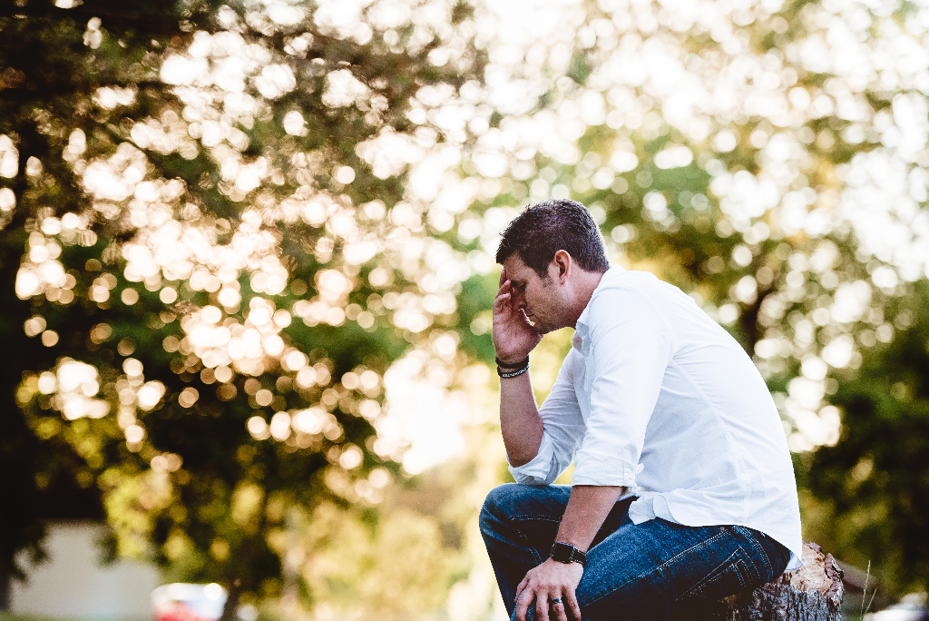 Man sitting down with face in hands with trees in the background